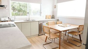 Et moderne køkken med spiseplads, hvide skabe, et stort vindue og et træspisebord med stole.