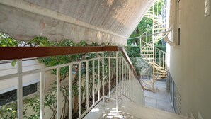 A staircase with white railings and a wooden handrail, leading to an outdoor area with greenery and a spiral staircase. - Retro 2-Bdrm House Near Metro in Heraklion by ΜΡS (Iraklio)