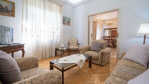 A living room with a sofa, armchairs, a coffee table, a television, and a dining area in the background. - Retro 2-Bdrm House Near Metro in Heraklion by ΜΡS (Iraklio)