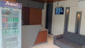 Un espace d’accueil comprenant un réfrigérateur rempli de boissons, un comptoir en bois et un canapé gris.