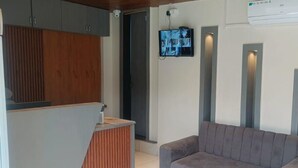 Un espace d’accueil comprenant un canapé, un téléviseur fixé au mur et un meuble en bois.