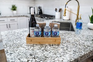 Una encimera de cocina con una caja de madera que contiene una botella de vino Coni, cuatro botellas de agua y una botella azul.