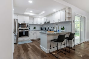 Una cocina moderna con armarios blancos, electrodomésticos de acero inoxidable, encimera de granito y una barra con dos taburetes.