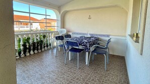 A covered outdoor area with a tiled floor, a table with chairs, and a view of buildings through large windows. - Charming 2-bedroom terrace apartment in amazing Vir, Walk to North&South Beaches (Vir)