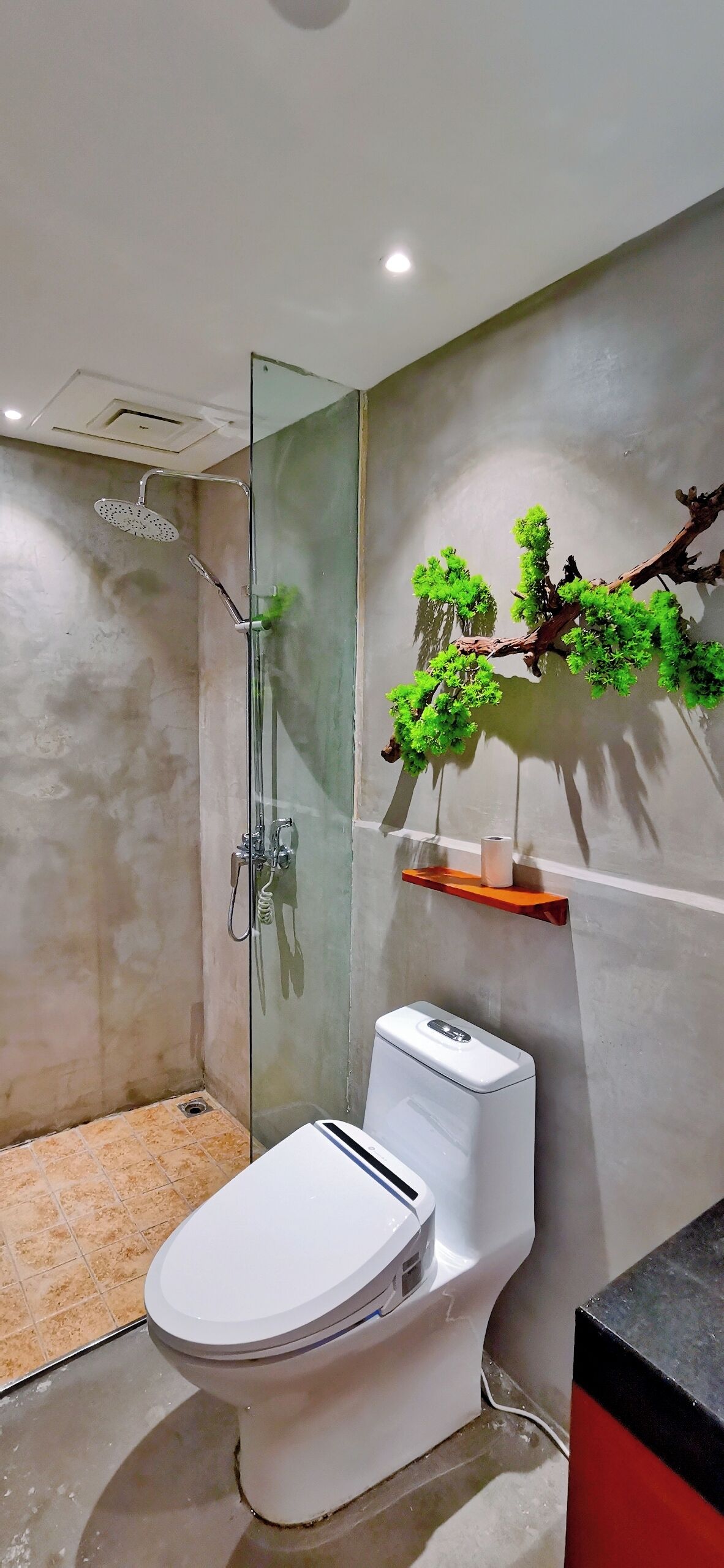 Un baño moderno con ducha de vidrio, inodoro y estante en la pared con una rama decorativa.