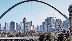 Un paisaje urbano con un puente arqueado destacado al frente y edificios altos al fondo.