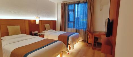 A hotel room with two beds, a desk, a chair, and a TV.