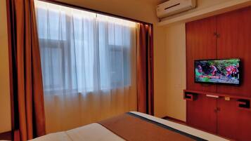Quarto de hotel com uma cama, uma televisão fixada na parede e uma janela com cortinas.