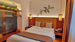 Una habitación de hotel con cama, mesitas de noche, espejo, planta colgante y armario.
