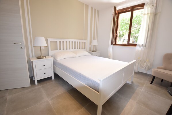 Une chambre à coucher avec un lit, deux tables de chevet avec des lampes, une chaise et une fenêtre avec des rideaux.