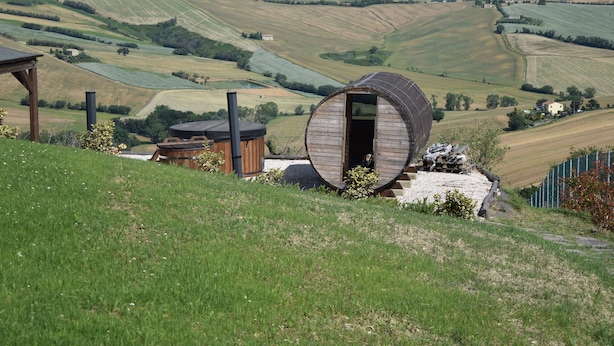 A rustic cabin with a circular wooden structure, surrounded by rolling hills and fields. - Casa In Collina (Terre Roveresche)