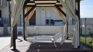 A covered outdoor seating area with a wooden deck and white lounge chairs. - Casa In Collina (Terre Roveresche)