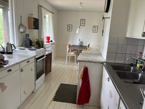 A kitchen with a stove, sink, and a dining area with a table and chairs. - 5 Person Holiday Home in Varmdo (Värmdö)