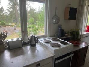 A kitchen with a gas stove, a kettle, and a window overlooking a garden. - 5 Person Holiday Home in Varmdo (Värmdö)