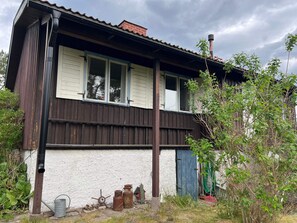 A two-story house with a white exterior and dark wooden trim. There is a visible chimney on the roof, and the house has a single visible window on the upper floor. - 5 Person Holiday Home in Varmdo (Värmdö)