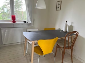 Un comedor con una mesa y sillas, una ventana con cortinas, un radiador y una lámpara fijada a la pared.