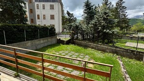 A courtyard with a wooden bench, a grassy area, and a building with multiple windows.