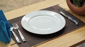 Une table à manger avec une assiette blanche, une fourchette, un couteau et une serviette bleue.