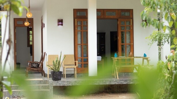 Une maison traditionnelle en bois, dotée d’un porche, de deux chaises, d’une table et d’une plante en pot.
