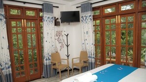 Une chambre d’hôtel avec un lit, deux chaises, une télévision et de grandes fenêtres avec des rideaux.