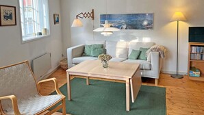 A living room with a sofa, a coffee table, a chair, a floor lamp, a painting, and a bookshelf. - 6 Person Holiday Home in Svaneke (Svaneke)