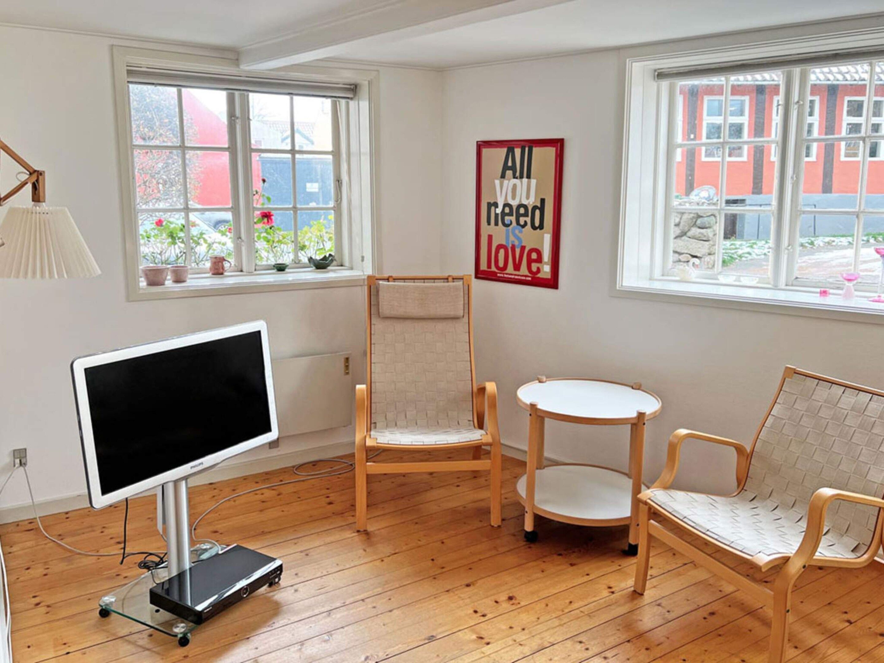 A room with a large flat-screen TV, two wooden chairs, a small round table, and a poster on the wall.