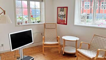 A room with a large flat-screen TV, two wooden chairs, a small round table, and a poster on the wall.