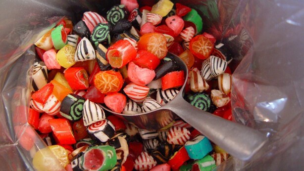 A variety of colorful candies in a transparent container with a spoon.