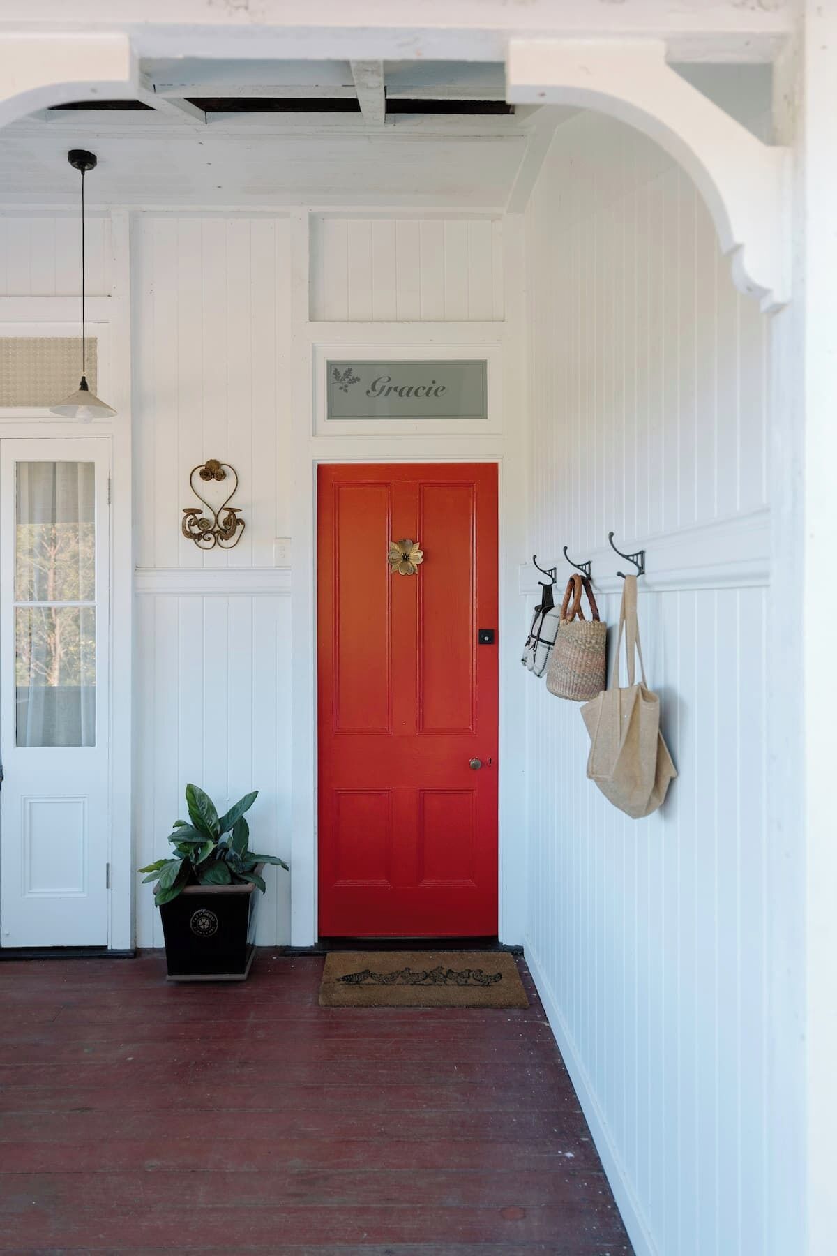 A hallway with a red door, a potted plant, a hanging bag, and a sign above the door.