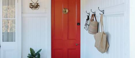 A hallway with a red door, a potted plant, a hanging bag, and a sign above the door.
