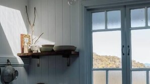 A kitchen with a window, a shelf with dishes, and a kettle.