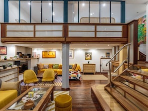 Amplia sala de estar con techo alto, muebles de madera y una escalera que conduce a un nivel superior.