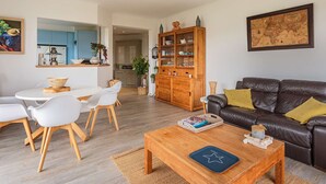 A modern living room with a wooden coffee table, a leather sofa, and a dining area with white chairs. - Apartment with port view, parking, near the beach (Hendaye)