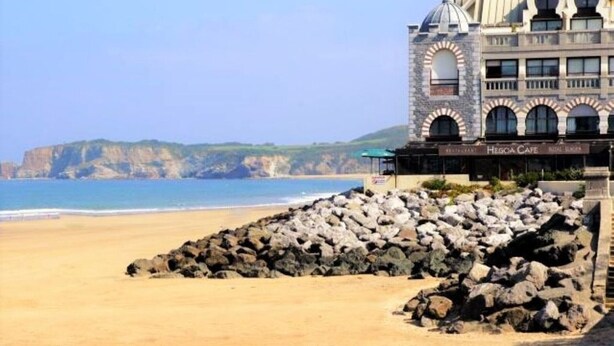 A coastal hotel with a stone facade, a beach view, and a rocky shoreline. - Apartment with port view, parking, near the beach (Hendaye)