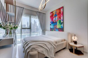 A modern bedroom with a city view, a bed, a bedside table, and a painting.