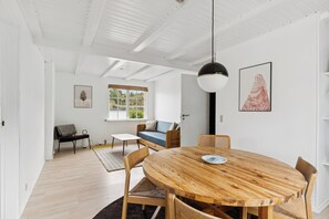 A room with a wooden dining table, chairs, a sofa, a window, and a hanging pendant light.