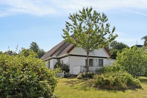 A single-story house with a sloped roof, surrounded by a well-maintained garden and a white picket fence.