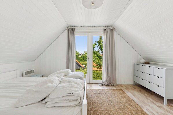 A bedroom with a bed, a dresser, a window, and a view of greenery outside.