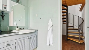 A bathroom with a sink, mirror, towel rack, and a spiral staircase.