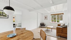 A modern interior with a wooden dining table, a sofa, and a window with blinds.