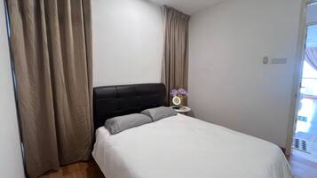 Ein Schlafzimmer mit Bett, Vorhängen, einem Nachttisch mit Spiegel und einer kleinen Vase mit Blumen.