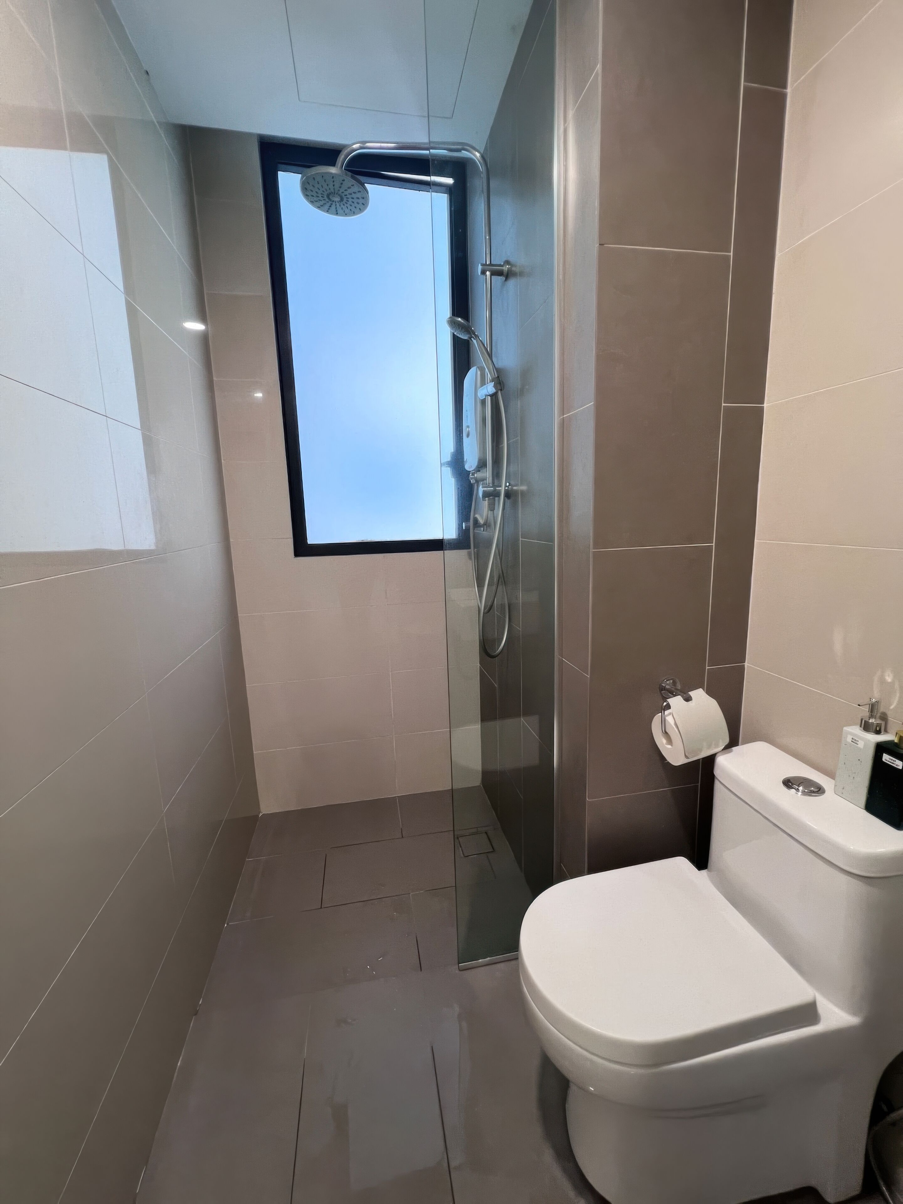 Een moderne badkamer met een douchecabine van glas, een toilet en een raam voor natuurlijk licht.