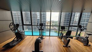 A modern gym with large windows, wooden flooring, and various exercise equipment. - KL Staycation Gateway Residences (Kuala Lumpur)