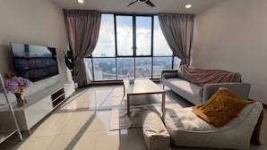 A modern living room with a large TV, a sofa, a coffee table, and a view of the city through large windows. - KL Staycation Gateway Residences (Kuala Lumpur)