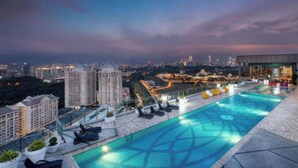 A rooftop infinity pool with a city view, lounge chairs, and potted plants. - KL Staycation Gateway Residences (Kuala Lumpur)