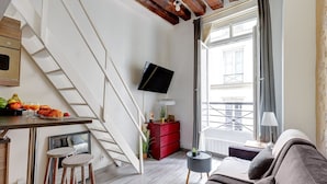 A modern living room with a staircase, a flat-screen TV, a sofa, and a dining area with stools and a fruit bowl.