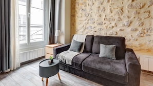 A modern living room with a dark grey sofa, a small round side table, a lamp, and a stone wall.