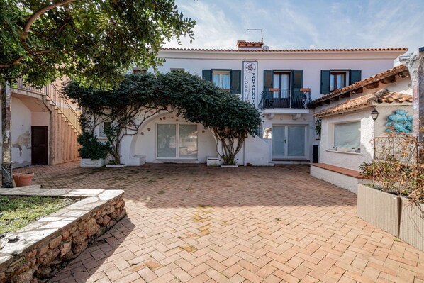 A courtyard with a paved floor, a building with a balcony, and a sign that reads "TARAGNI Locanda". - Locanda Tartarughino - Suite Luna (Porto Rotondo)