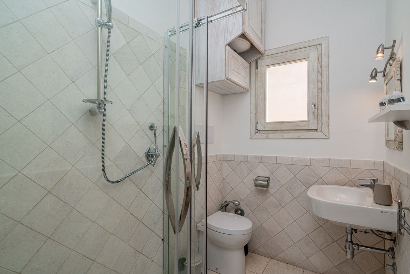 Un baño con ducha de vidrio, inodoro y lavamanos con espejo.