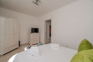 A bedroom with a bed, white wardrobe, television, and a door leading to another room. - Locanda Tartarughino - Suite Luna (Porto Rotondo)